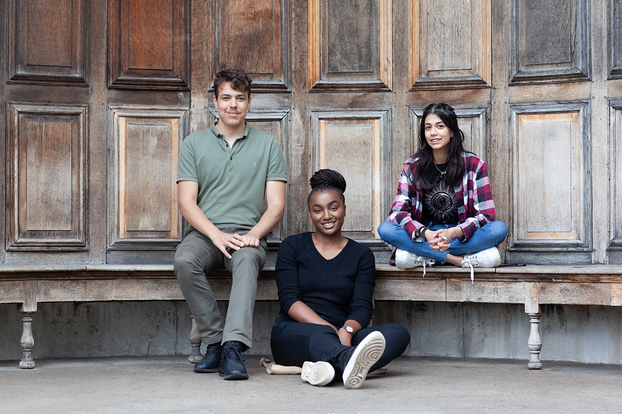 Three young people from the EY Foundation programmes are sat together on a bench.